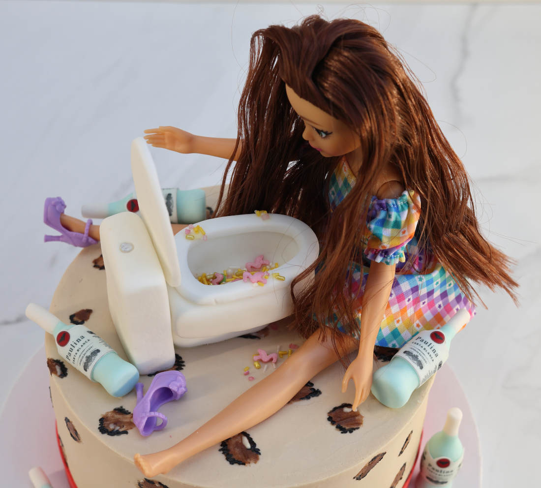 Lėlė sėdi ant torto šalia unitazo